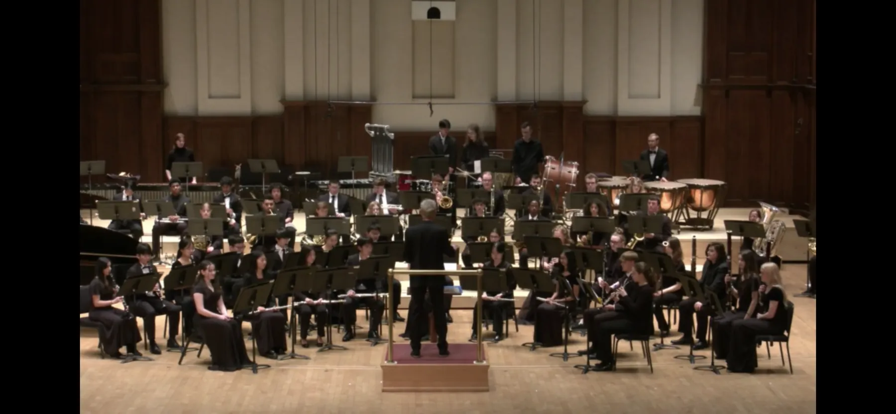 Concert band performing in an auditorium under the direction of a conductor