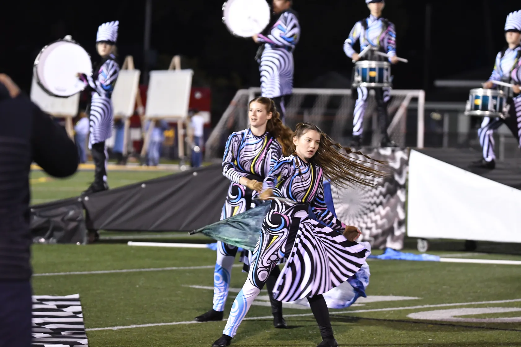 South Lyon Color Guard performer with marching percussion behind at a 2025 show