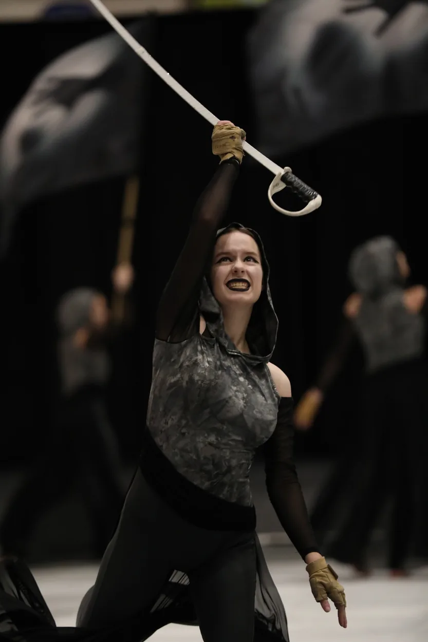 South Lyon Color Guard performer raising a saber during an indoor performance; specific season unverified